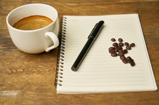 coffee, notepad, pen and coffee beans on table